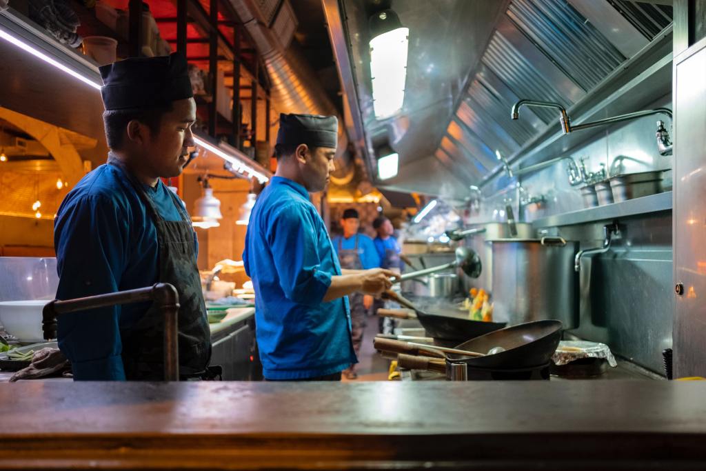Two chefs in proper uniform with hairnet preparing orders in the commercial kitchen.